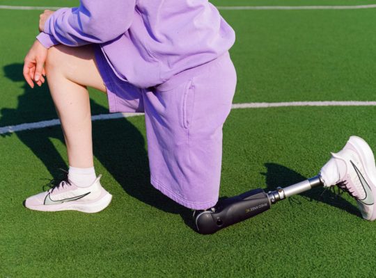 Une sportive avec une jambe bionique se tient à genoux sur un terrain de sport